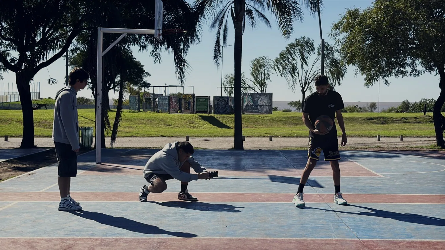 Rodaje de día en una cancha de básquet: el camarógrafo agachado filmando a un jugador con la pelota