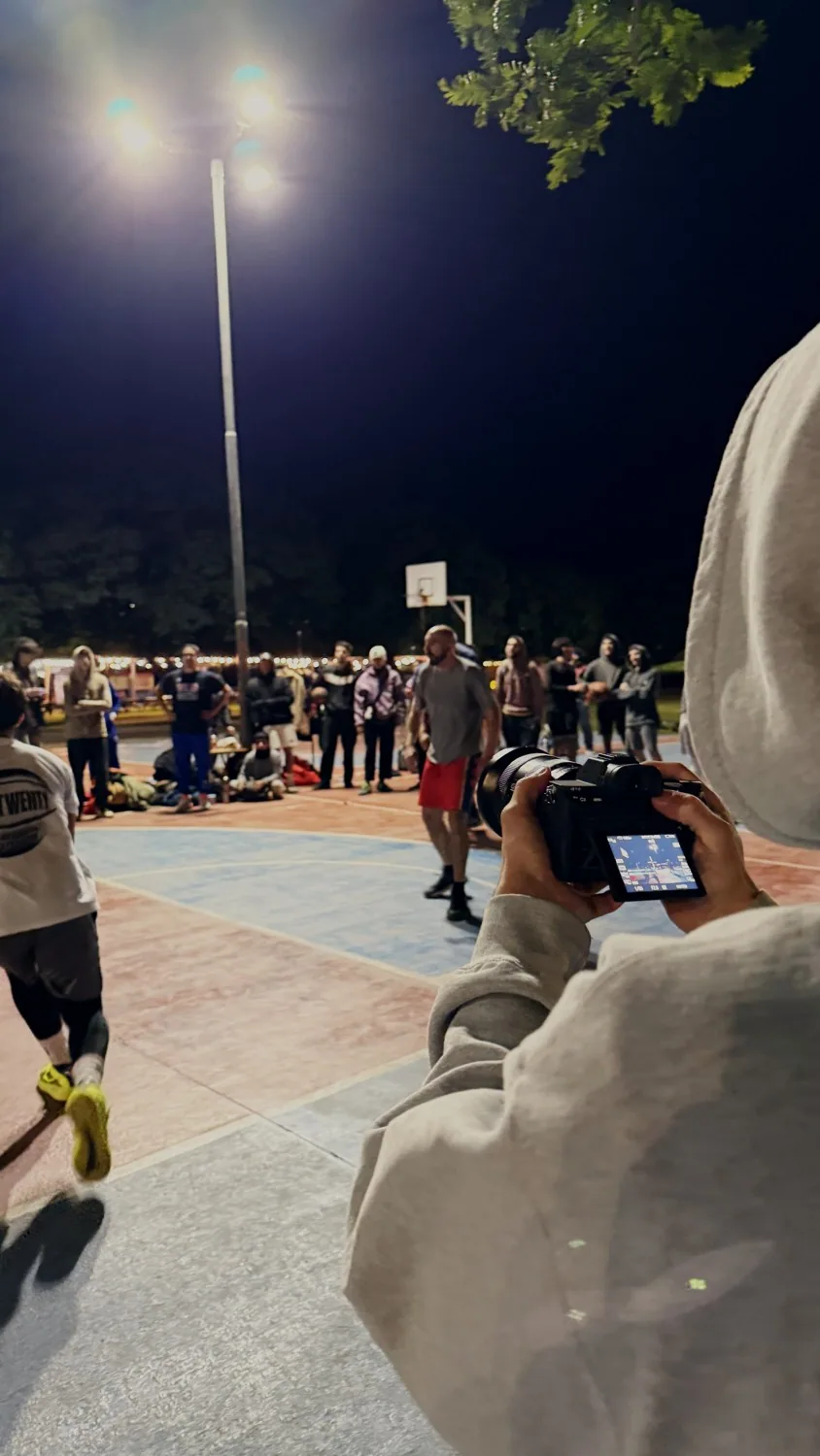 Rodaje nocturno en una cancha de básquet llena de gente, visto por encima del hombro del camarógrafo